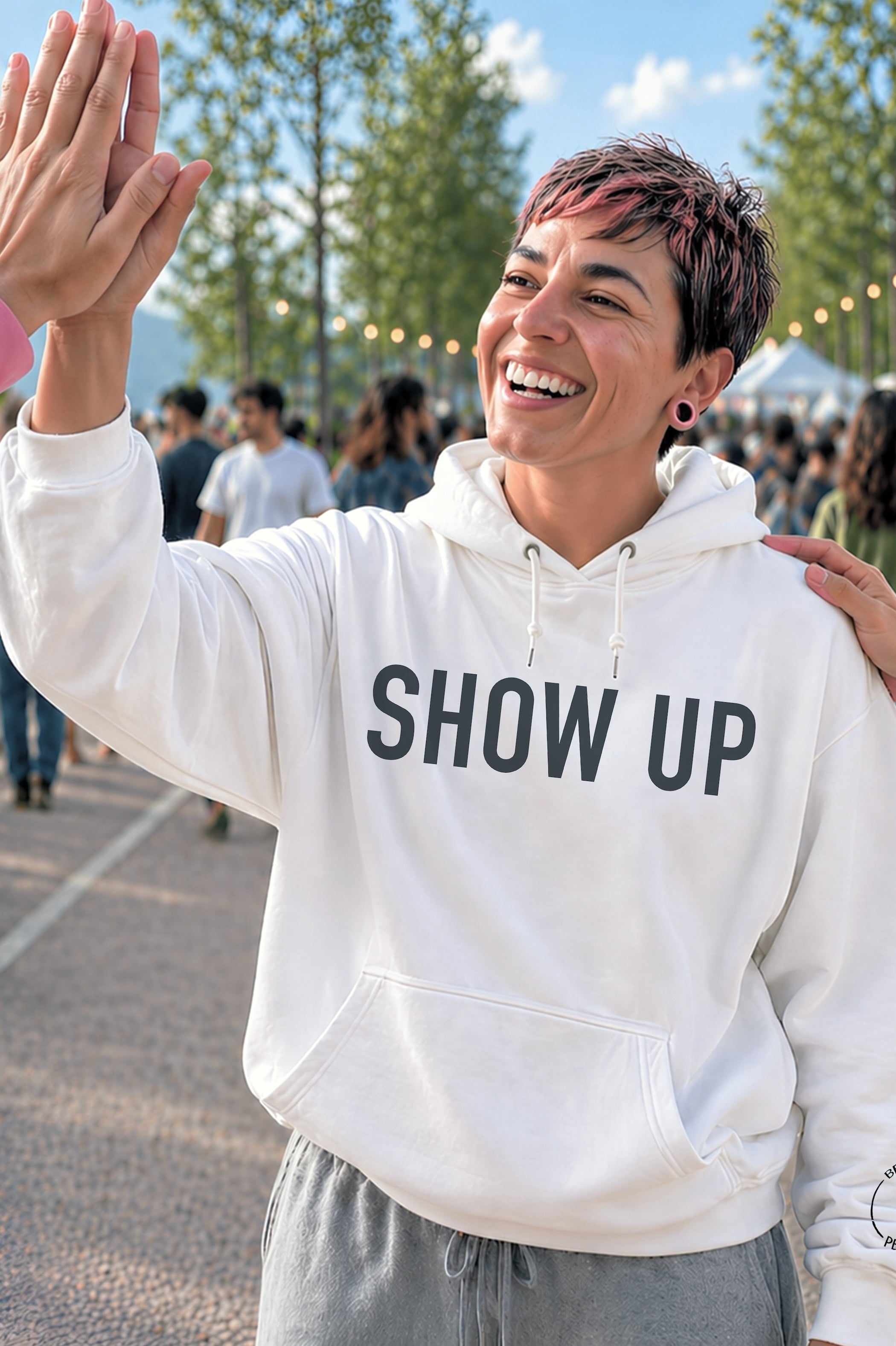 Model wearing a white unisex hoodie featuring a bold gray Show Up graphic while giving a high five, created by content creators Kayla and Samantha.