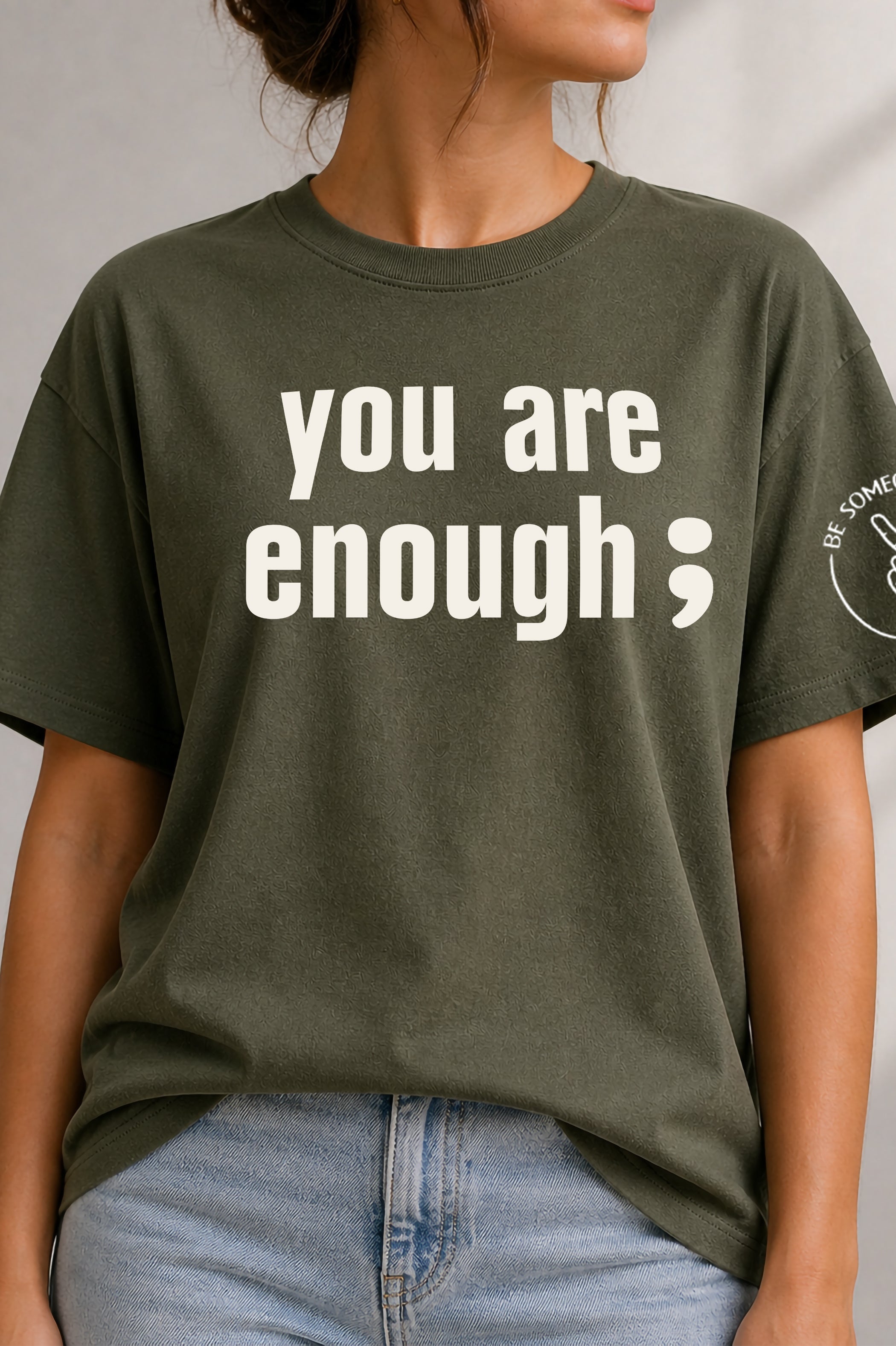 Model wearing an olive green unisex t-shirt featuring the text graphic You Are Enough with a semicolon from Be Someone's Person, created by Kayla and Samantha.